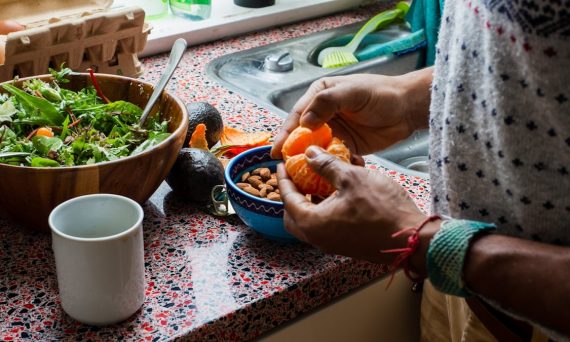 person holding orange fruit on blue ceramic bowl